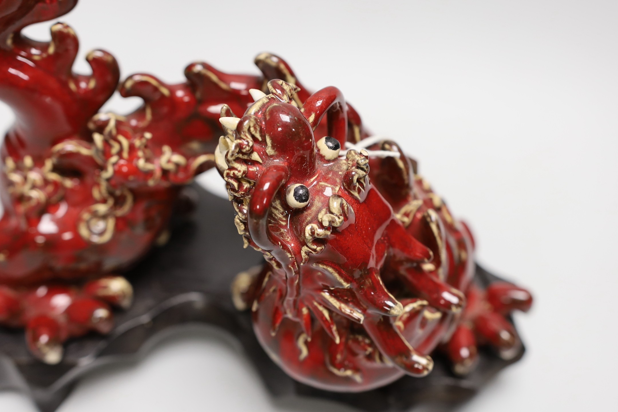 A Chinese red glazed figure of a dragon, on hardwood stand. 28cm wide